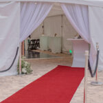 A luxurious red carpet guided guests to a pristine white tent with elegant draped curtains, perfectly situated on a brick pathway in Atlanta. Classic stanchions with ropes added a touch of sophistication to the entrance. Within the spacious tent, tables were tastefully set up with minimal decor, creating an ideal ambiance for formal events. All of these elements were expertly provided by T3 Event Rentals, your trusted partner for event rentals throughout Atlanta.