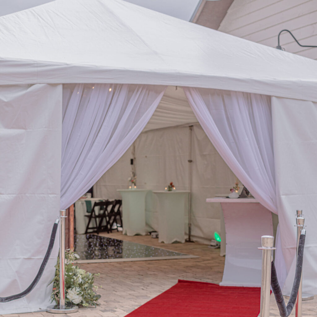 A luxurious red carpet guided guests to a pristine white tent with elegant draped curtains, perfectly situated on a brick pathway in Atlanta. Classic stanchions with ropes added a touch of sophistication to the entrance. Within the spacious tent, tables were tastefully set up with minimal decor, creating an ideal ambiance for formal events. All of these elements were expertly provided by T3 Event Rentals, your trusted partner for event rentals throughout Atlanta.
