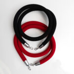 Two elegant black or red velvet ropes, each 8 long and featuring shiny metal clips at both ends, are stylishly intertwined on a white surface, creating an eye-catching pattern for events in Dawsonville. T3 Event Rentals offers these exquisite ropes as part of their rental collection. Enhance your Dawsonville event with the sophisticated touch of velvet ropes from T3 Event Rentals.
