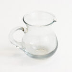 The Glass Creamer, with its clear round design, short spout, and curved handle, elegantly sits on a white surface at an event in North Georgia. Enhance your gatherings with rentals from T3 Event Rentals.