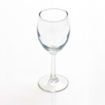 An Optic White Wine Glass (25 rack) with a clear, empty bowl is elegantly poised on its slender stem and round base against a simple white backdrop in Atlanta. Elevate your next event with T3 Event Rentals, specializing in top-quality glassware rentals across the city.