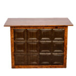 Experience the charm of The Tin Bar, a small wooden bar designed with a flat rectangular top and featuring square panel designs at the front, perfect for any rustic-themed event in Atlanta. Its natural finish highlights the woods authentic texture and grain, creating a simple yet captivating appearance. Available exclusively for rent through T3 Event Rentals.