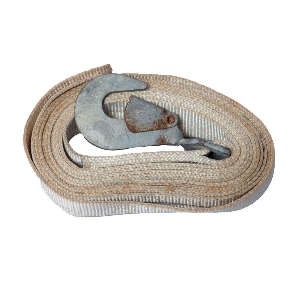 A rugged beige ratchet strap, coiled and featuring a metal hook on one end, is showcased against a white background. The straps wear and the rust on the hook make it perfectly suited for rental purposes. Ideal for those in the Dawsonville area seeking reliable equipment.