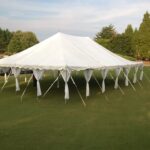 A 20 Rope and Pole Tent, courtesy of T3 Event Rentals, graces the grassy lawn under a clear Atlanta sky. With open sides revealing a lush green landscape, its ideal for creating memorable events. Perfect for rentals in the Atlanta area!.