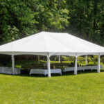 A spacious white 10 Frame Tent from T3 Event Rentals is elegantly set up on the lush lawns of Dahlonega. Beneath, tables adorned with crisp white tablecloths create a sophisticated outdoor ambiance. The backdrop of dense green trees enhances the tranquil setting, making it perfect for events in and around Dahlonega. All items featured here are available for rent through T3 Event Rentals.