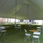 T3 Event Rentals offers an elegant setup with a 20 Rope and Pole Tent, featuring a pristine white canopy over round tables and folding chairs set on lush grass in Forsyth County. The backdrop of a building with stairs adds to the sophisticated ambiance. Perfect for your next event, these rentals are ideal for creating unforgettable moments in Forsyth County.