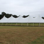 Set on a lush grassy field in Forsyth County, with an overcast sky and trees providing a scenic backdrop, this 20 Rope and Pole Tent by T3 Event Rentals features multiple peaks. Its the perfect setting for your next event. Remember, all items are rentals from T3 Event Rentals, your go-to choice for tent rental services across Forsyth County!.