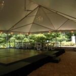 Discover the perfect indoor stage for rent in Atlanta, set on a charming brick patio adorned with abundant white chairs and tables. Ideal for events in North Georgia, this venue is nestled amidst lush greenery and features elegant chandeliers hanging from the ceiling. Conveniently located near Forsyth County, Dawsonville, Dahlonega, and Marietta, its an exceptional choice for your next occasion.