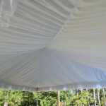 Discover the elegance of T3 Event Rentals as you gaze up at a billowing fabric ceiling beneath our stunning tent liners, with the lush trees and greenery of Dawsonville providing a breathtaking backdrop. Perfect for any event in this charming area.