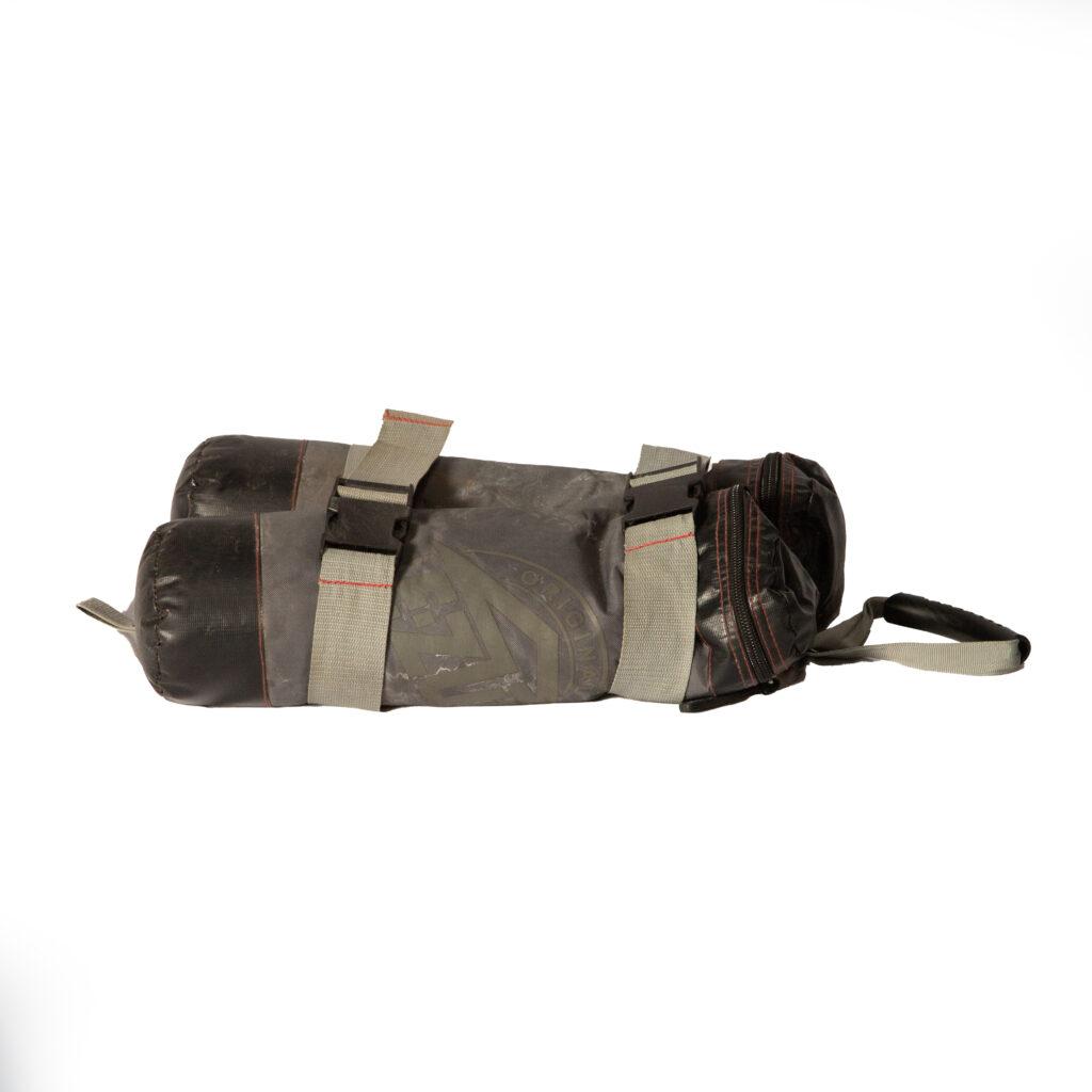 Discover the ultimate workout accessory with T3 Event Rentals in Atlanta: the 45Lbs Pop Up Sand Bag. This sleek black, cylindrical bag features two main compartments and is secured by durable gray straps with striking red stitching. Its top handle and adjustable loops provide maximum convenience, making it a perfect fit for any event in Forsyth County or a rugged adventure near Dahlonega. Available exclusively for rental, this sandbag stands out against its plain white background as a versatile option for events throughout North Georgia. Rely on T3 Event Rentals to enhance your next fitness event or training day in Dawsonville.