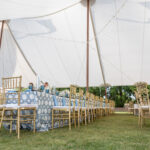 Experience a stunning outdoor event in North Georgia with T3 Event Rentals sailcloth rope and pole tent, creating a beautiful cover for your celebration. Our gold chairs and long tables—dressed in elegant blue-patterned tablecloths and white floral arrangements—are perfect for events on a grassy lawn. All event furniture, tents, and décor are available exclusively for rent from T3 Event Rentals in North Georgia—nothing is for sale. Let T3 Event Rentals bring your dream event to life!.