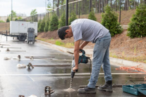 In the heart of Atlanta, a man clad in a gray T-shirt and jeans expertly handles a power drill on the damp pavement. He is surrounded by an array of tools and equipment from T3 Event Rentals, tailored for event success. In the background, trees and a fence create an idyllic setting alongside a utility truck that stands ready to address any needs for outdoor gatherings. While these high-quality items are available exclusively for rent from T3 Event Rentals, they ensure your event in Atlanta runs smoothly without a hitch.