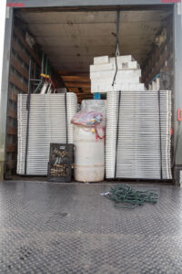 The image provides a glimpse into a truck filled with event rentals destined for Dahlonega. Inside, youll find stacks of white folding chairs, boxes on a sturdy platform, a plastic-wrapped barrel, and a secure crate. A bundle of tangled green cords is on the floor, primed for setup. All these items are available through T3 Event Rentals, your go-to source for event services across North Georgia.