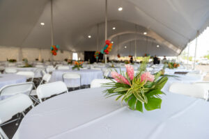 In the heart of Forsyth County, a spacious event tent by T3 Event Rentals showcases elegant round tables draped in white cloths and adorned with floral centerpieces highlighted by pink blossoms and lush greenery. Encircled by white chairs, the vibrant atmosphere is enhanced with brightly colored balloons in the backdrop, perfectly capturing the essence of T3 Event Rentals.