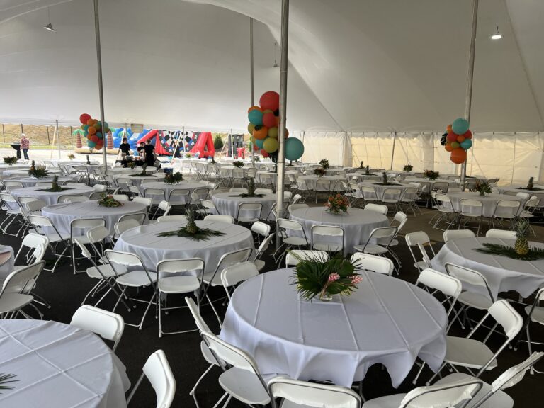 Transform an ordinary gathering into an extraordinary experience with T3 Event Rentals in Forsyth County. Our spacious white tent is equipped with round tables and elegant white folding chairs, setting the stage for a lively event. The tables are enhanced with tropical centerpieces featuring palm leaves and pineapples, while colorful balloons festively decorate the poles. Trust T3 Event Rentals to provide everything needed for a memorable celebration in Forsyth County. Remember, all items are rentals!.