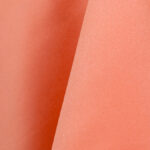 A close-up of Satin Coral Linens from T3 Event Rentals highlights the smooth folds and textured drape, perfect for events in Forsyth County. Subtle shadows enhance the elegance of this rental option, available exclusively through our services.