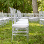 Clear acrylic chairs with white cushions from T3 Event Rentals set up in neat rows on lush green grass, surrounded by trees in North Georgia—perfect for an elegant outdoor wedding or ceremony. All rentals provided by T3 Event Rentals.