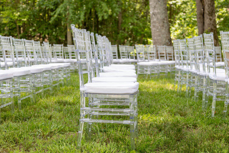 Clear acrylic chairs with white cushions from T3 Event Rentals set up in neat rows on lush green grass, surrounded by trees in North Georgia—perfect for an elegant outdoor wedding or ceremony. All rentals provided by T3 Event Rentals.
