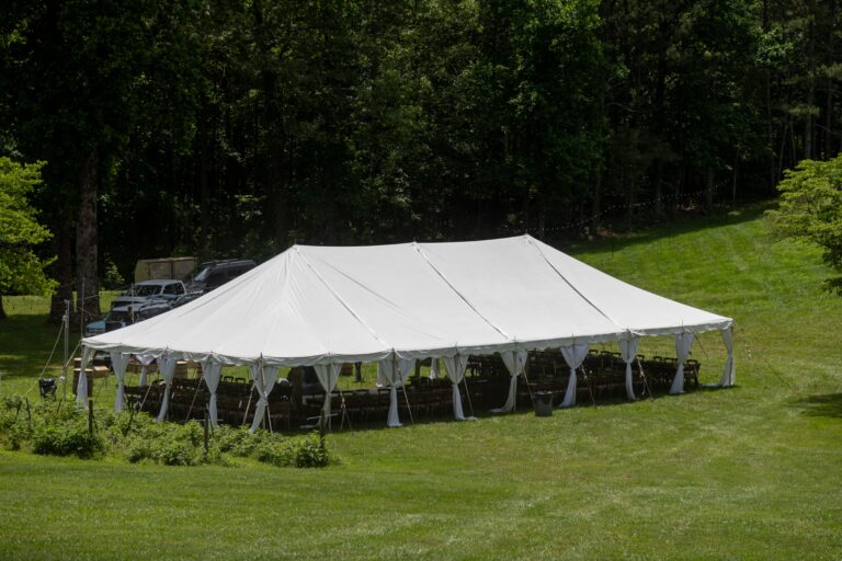 Heres an example rewritten for location SEO using Forsyth County: A spacious white event tent with open sides—perfect for outdoor gatherings—stands on a lush lawn surrounded by trees in Forsyth County. Under the tent, you’ll find rental tables and chairs from T3 Event Rentals, ready to welcome guests. A few cars are parked nearby, making access convenient. Trust T3 Event Rentals for all your tent and party rental needs in Forsyth County!.