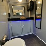 The 2 Stall Restroom Trailer from T3 Event Rentals is available for rent in Forsyth County. Perfect for local events, this luxury restroom trailer features modern gray cabinets, a sleek black countertop, blue accent lighting beneath the sink, comfortable round toilets, a spacious wall mirror, decorative basket on the counter, and an elegant wood-style floor. Contact T3 Event Rentals to reserve your restroom trailer rental in Forsyth County today! Let me know if youd like versions for different areas!.