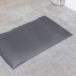 A black Anti-Fatigue Mat from T3 Event Rentals rests on light gray carpet near a white wall in Dahlonega, GA. Rentals only.