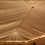 Twinkle lights rental for events – elegant string lighting creating a warm glow under a clear-top tent with decorated tables.