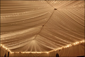Twinkle lights rental for events – elegant string lighting creating a warm glow under a clear-top tent with decorated tables.