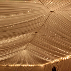 Twinkle lights rental for events – elegant string lighting creating a warm glow under a clear-top tent with decorated tables.