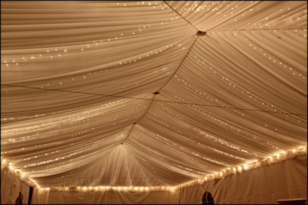 Twinkle lights rental for events – elegant string lighting creating a warm glow under a clear-top tent with decorated tables.