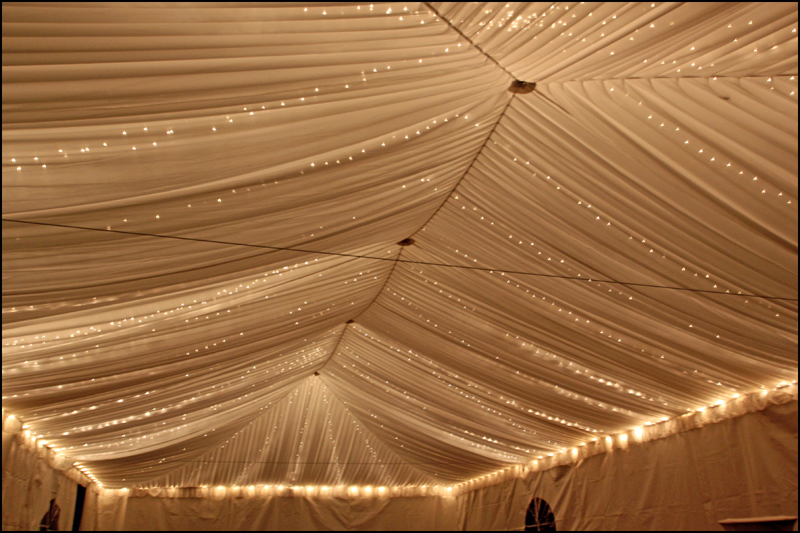 Twinkle lights rental for events – elegant string lighting creating a warm glow under a clear-top tent with decorated tables.