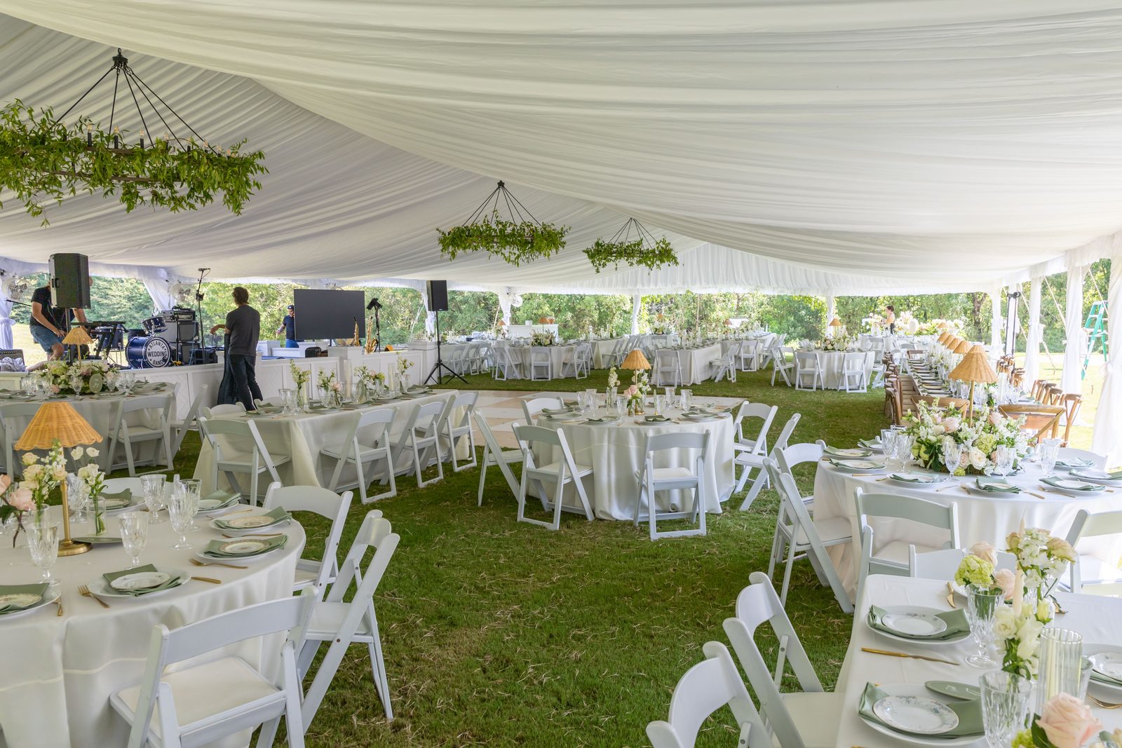 Wide view inside a 50' x 100' tent with a pleated ceiling liner, round reception tables and white resin chairs.