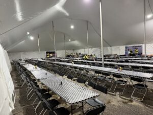 Lit dining tent with long rows of tables and chairs for utility crews