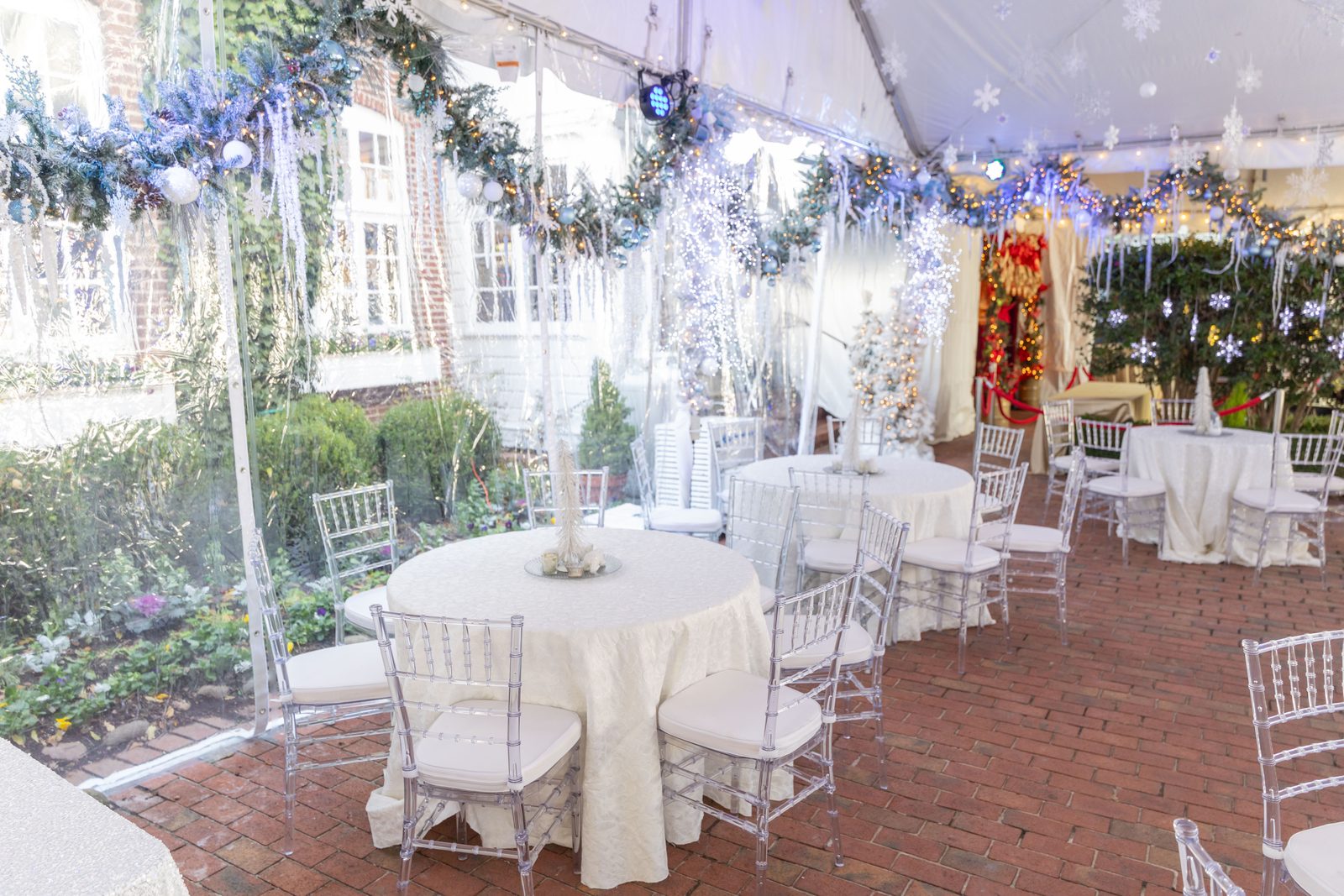 Round tables with white linens and clear chiavari chairs inside the heated tent, with daylight through clear sidewalls.