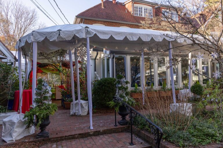 White frame tent with a scalloped valance beside a private home over a brick patio.