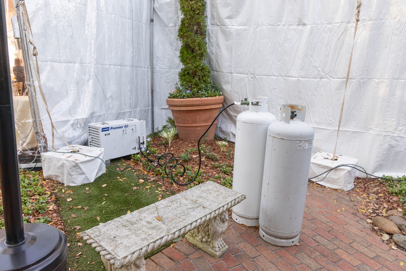 Tent heater outside the tent wall on a brick patio, with propane cylinders beside it.